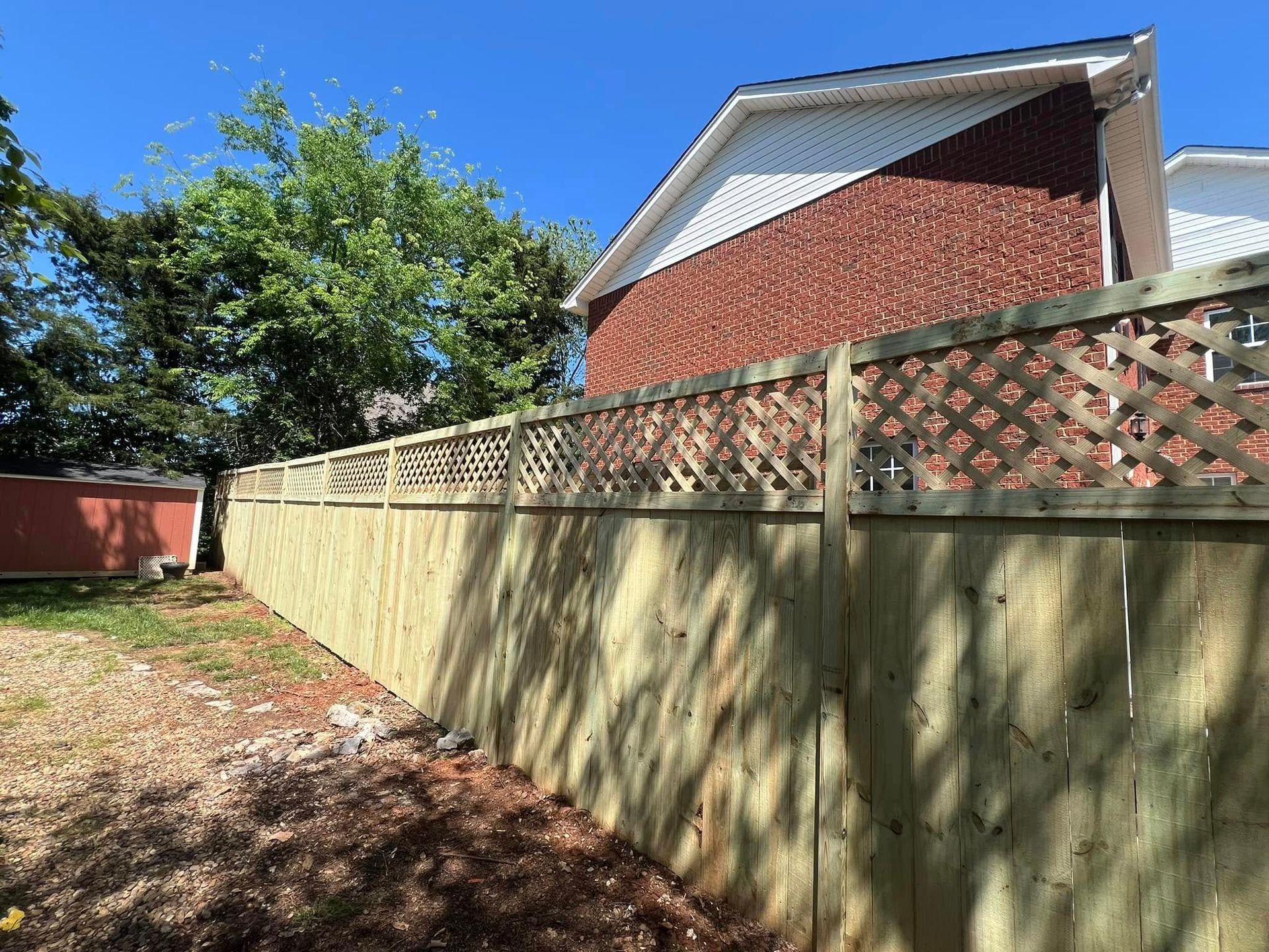 Wooden fence with lattice top along a yard with a brick building in the background.