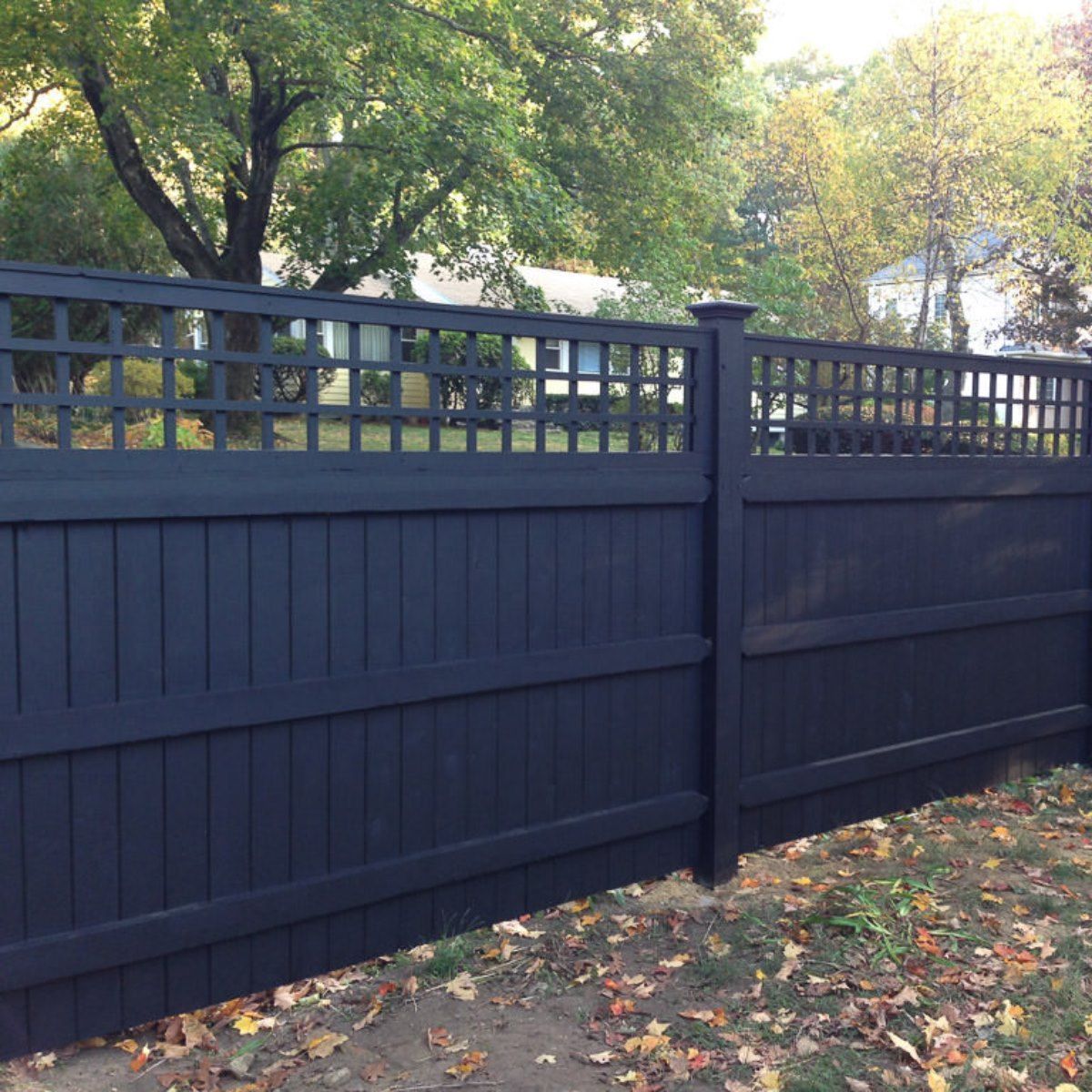 Black wooden fence with lattice detail, set outdoors near trees.