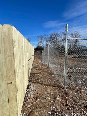 Wooden fence next to chain link fence with dirt path between them, against a blue sky.