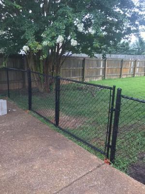 Black chain-link fence along a concrete patio, with a tree and wooden fence in the background.