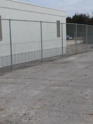 Chain-link fence bordering a white modular building in an outdoor, gravel area.