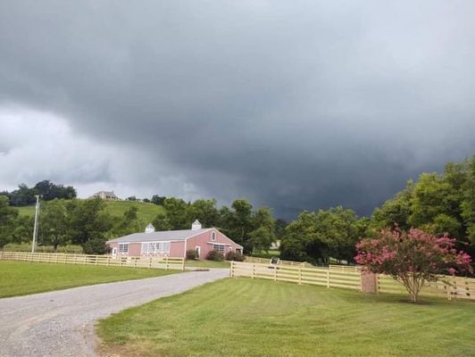 Stormy sky looms over a pink building, green lawn, and wooden fence.