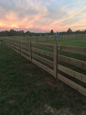 Wooden fence in a grassy field at dusk, with pink and orange sky.