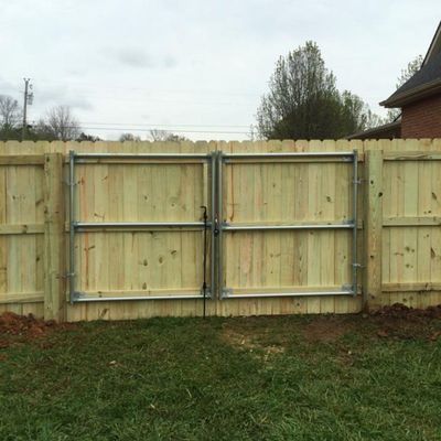 Wooden fence with double gates in a grassy yard, overcast sky.