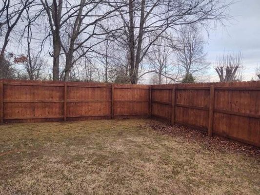 Wooden fence enclosing a yard of dry grass, bare trees in the background under a cloudy sky.