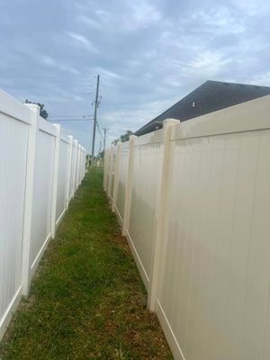A narrow grassy walkway between two white vinyl fences under a cloudy sky.