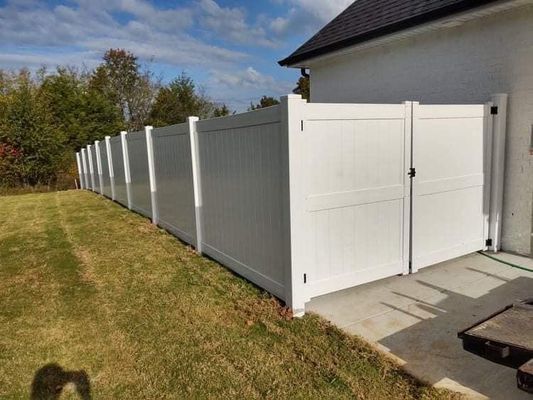 White vinyl fence along a grassy yard and house with a gate, under a blue sky.