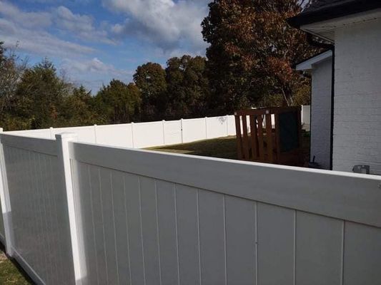 White vinyl fence surrounding a backyard with a house on the right.