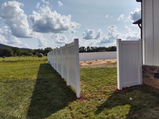 White vinyl fence with a gate, framing a grassy yard under a cloudy sky.