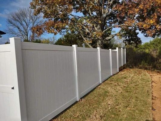 White vinyl fence along a grassy area, autumn trees in the background.