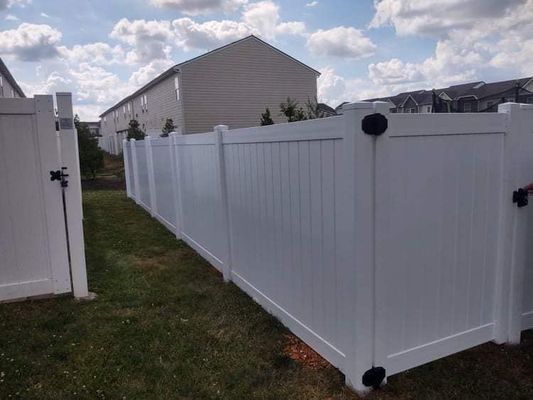 White vinyl fence in a backyard, with a gate open, under a cloudy sky.
