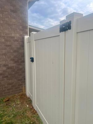 White vinyl fence with a gate next to a brick wall and grass. A black latch and hinges are visible.