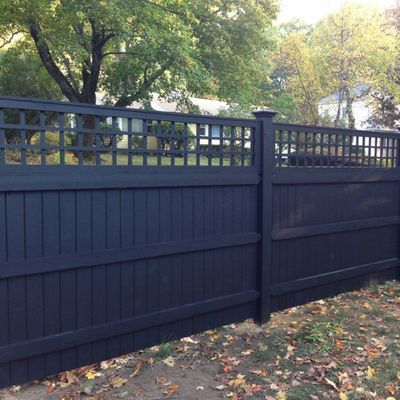 Black wooden privacy fence with lattice top, in a yard with trees.