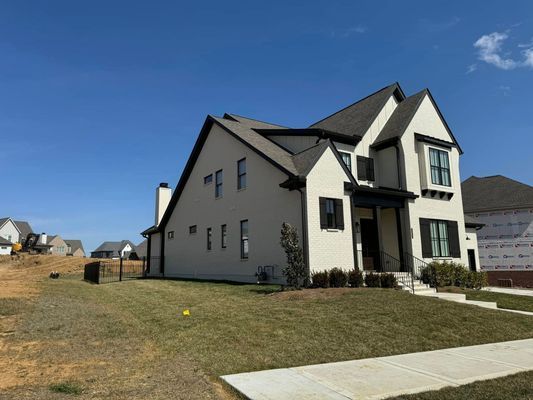 Modern two-story house with light stucco walls, dark trim, and a dark roof on a sunny day.