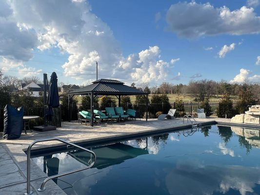 Poolside gazebo with turquoise cushions, pool, blue sky with clouds.