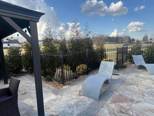 Patio with modern chaise lounges, black fence, and a gazebo in a sunny outdoor setting.
