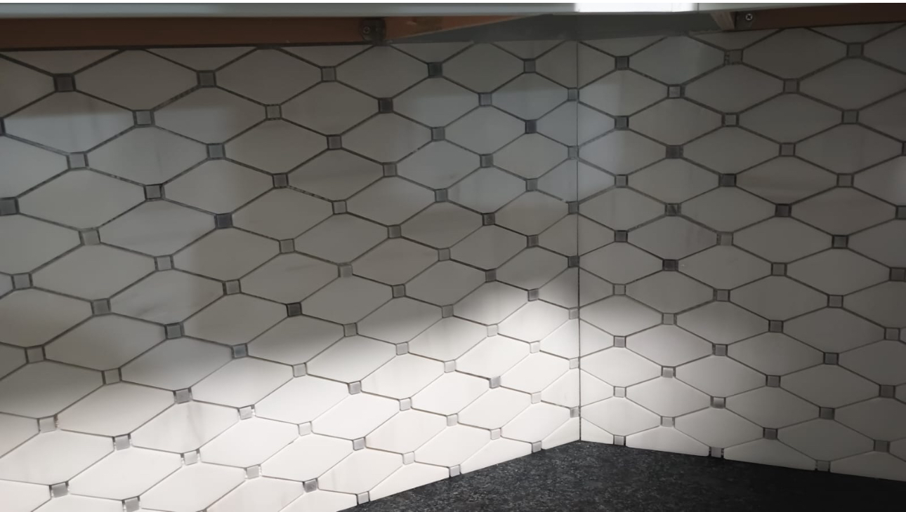 Tiled wall corner. White diamond-patterned tiles with gray accents meet at a right angle. A dark surface is below.