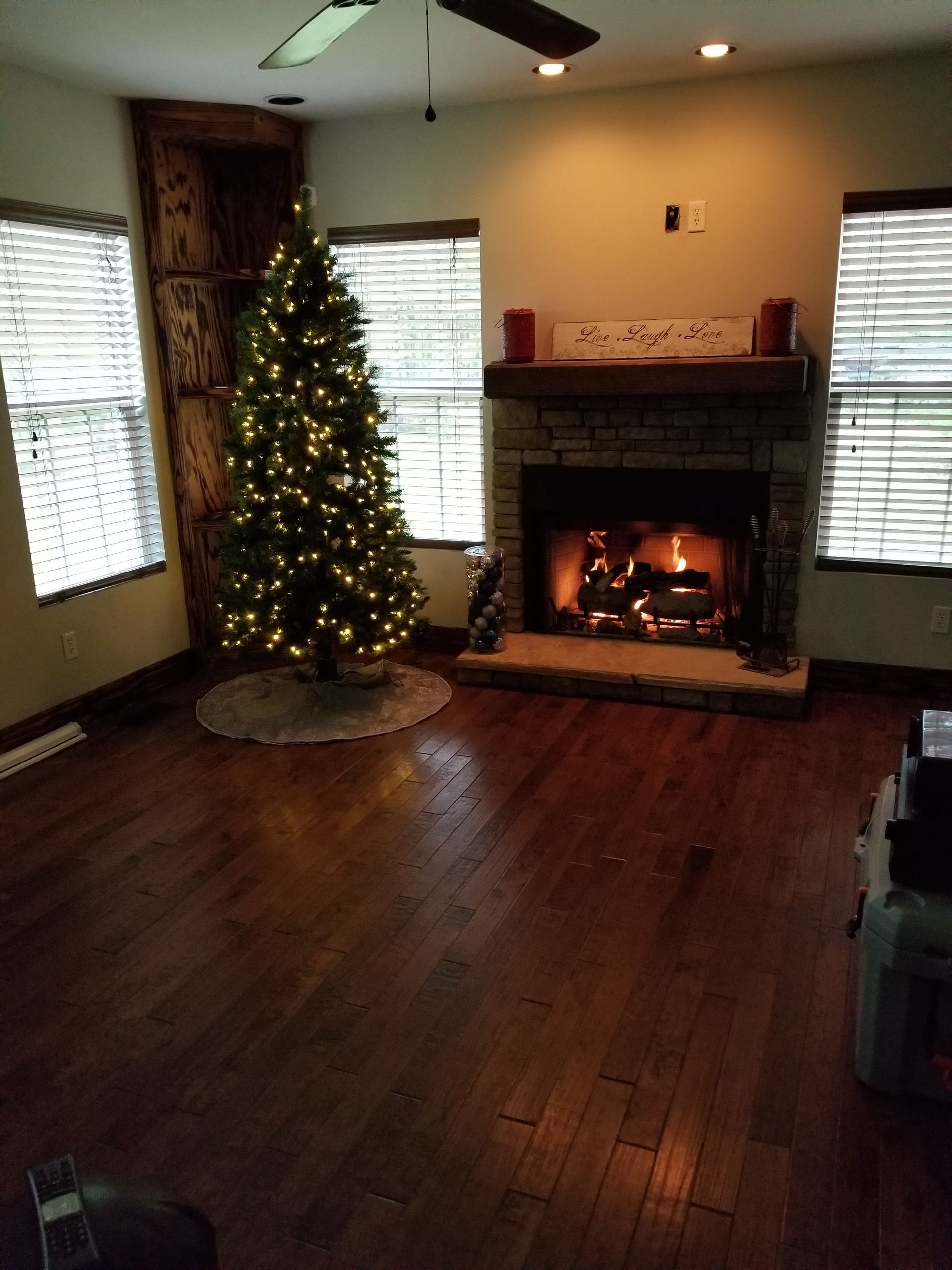 Living room with a lit Christmas tree next to a built-in bookshelf, fireplace, and hardwood floors.