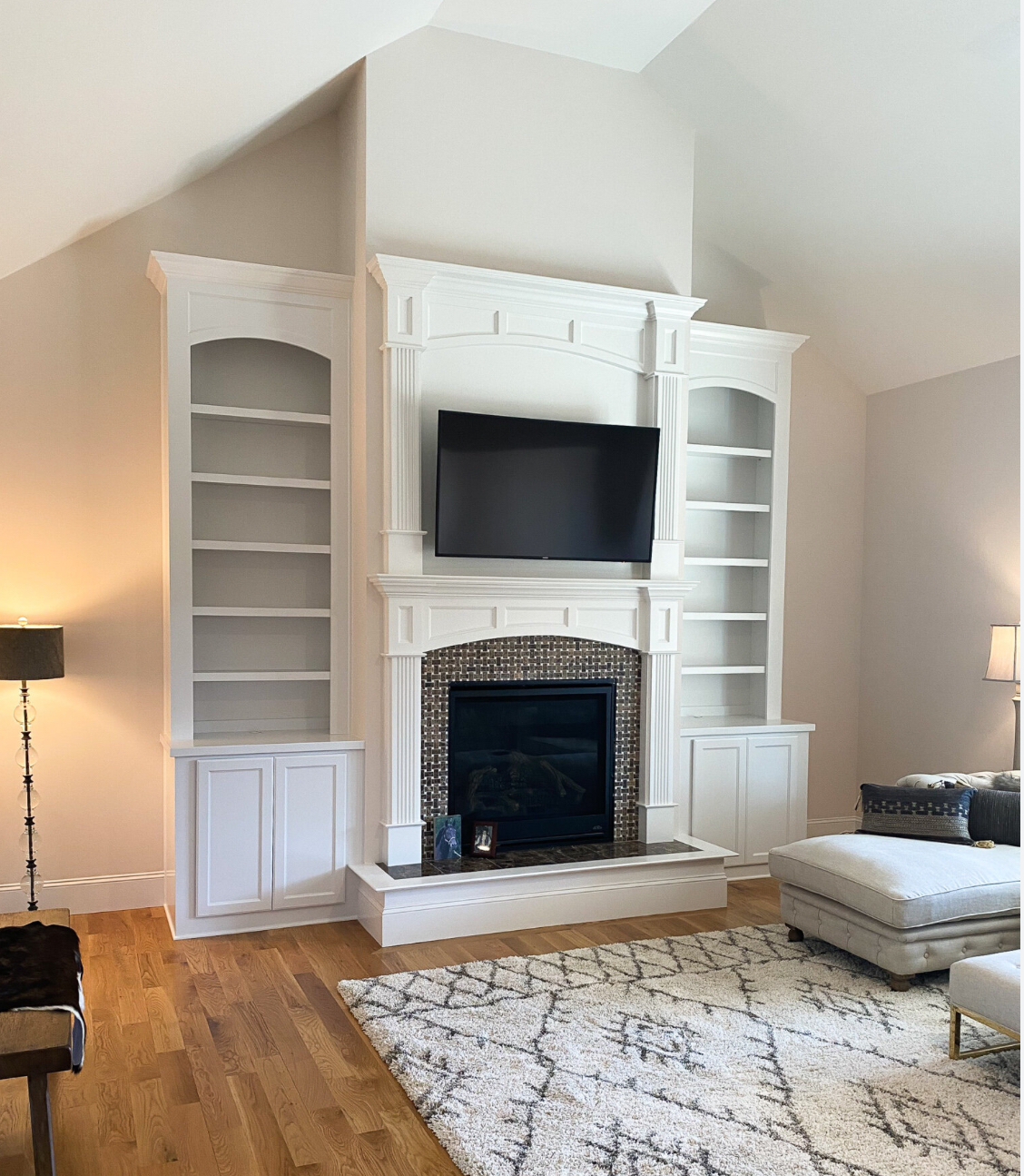 Living room with white fireplace, built-in bookshelves, and a mounted TV. Hardwood floors and a rug are visible.