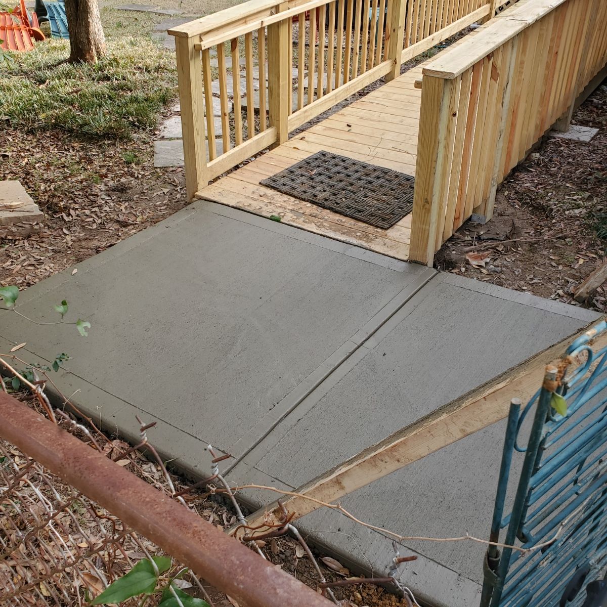 A wooden ramp with handrails leads to a raised wooden walkway. A concrete ramp leads up to it.