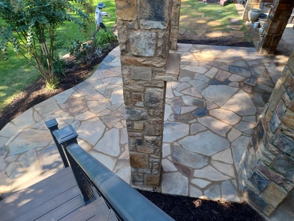 Stone patio and walkway with a brown and tan stone pillar. Dark brown mulch borders the walkway and garden.