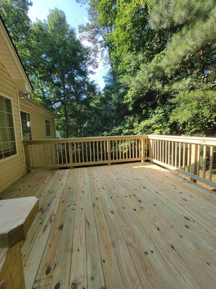 A wooden deck attached to a house, surrounded by a railing and overlooking a wooded area.