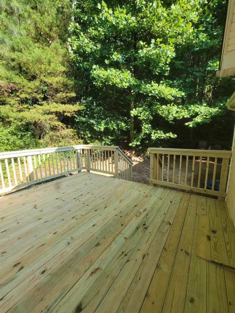 Wooden deck surrounded by railing, extending into a lush green forest. Sunny outdoor setting.