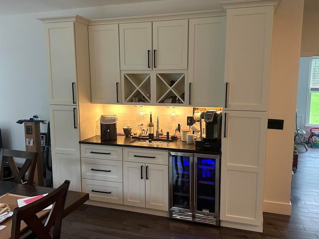 Built-in home bar with off-white cabinets, a black countertop, a wine fridge, and a coffee maker.