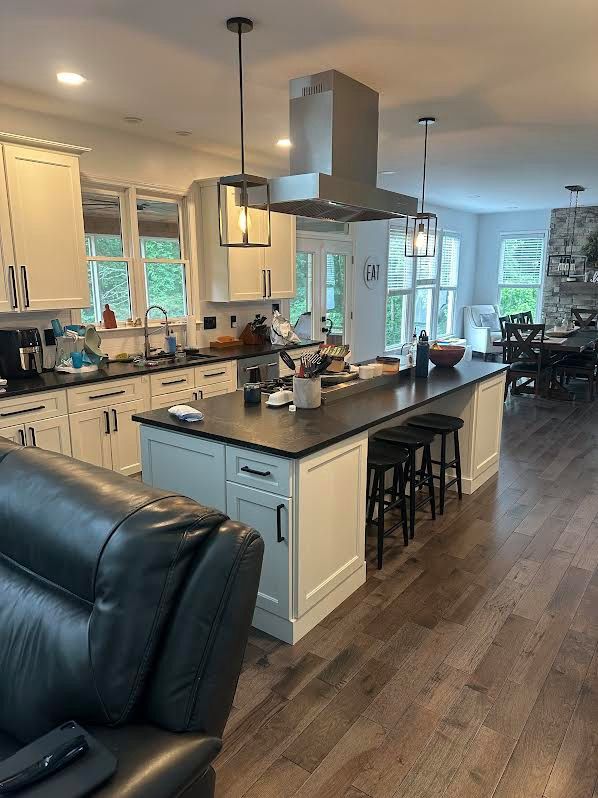Spacious kitchen with white cabinets, a black island, and stainless steel range hood. A black leather couch sits in the foreground.