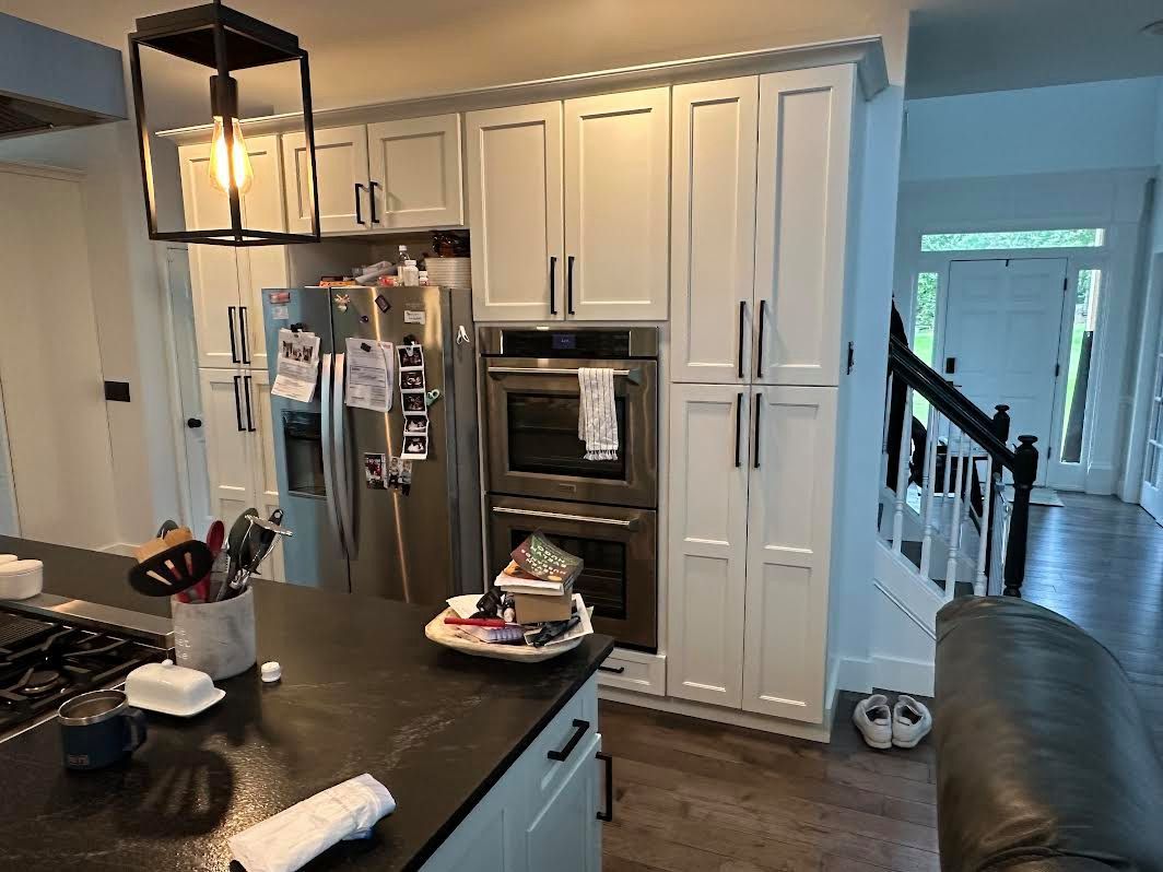 Kitchen with white cabinets, a stainless steel refrigerator, and a black countertop island. Sunlight streams in from a doorway.
