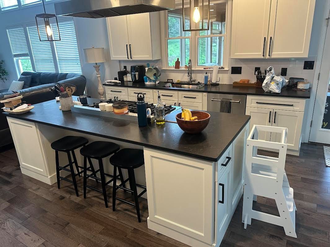 Modern kitchen with a black countertop island, white cabinets, and black stools. A small child's learning tower stands near the island.