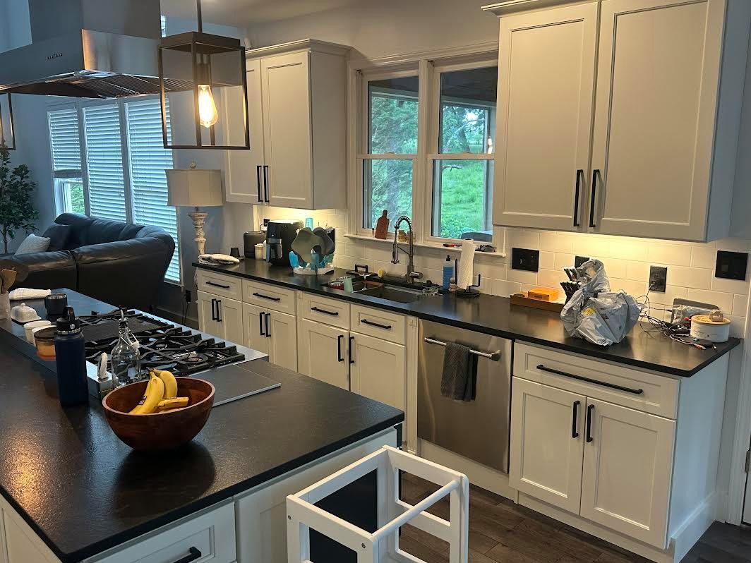 A bright kitchen with white cabinets, dark countertops, and a central island with a gas range. A bowl of bananas sits on the island.