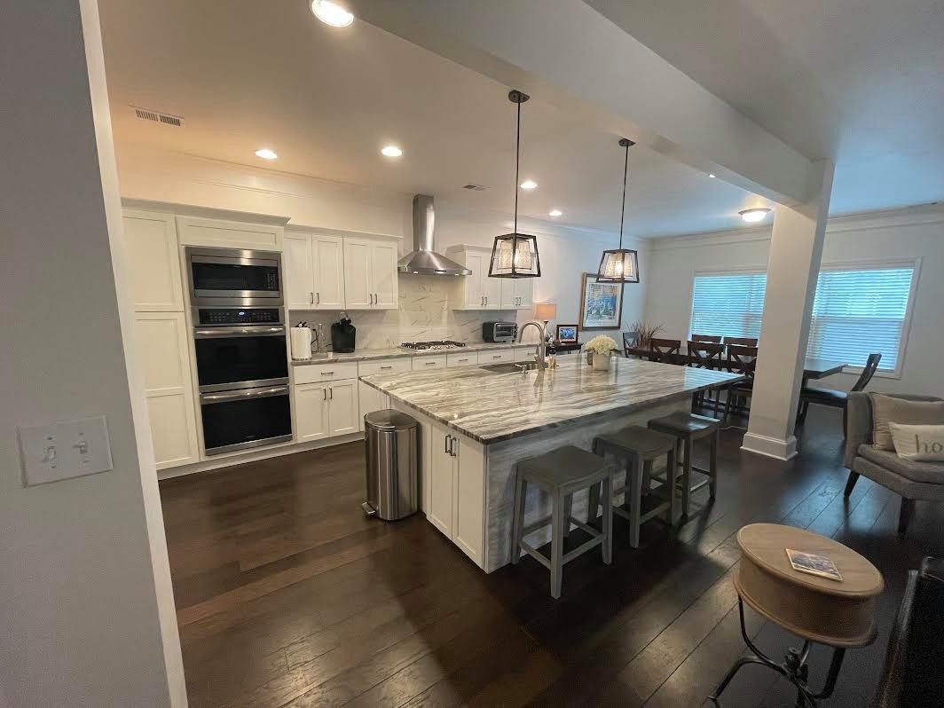 A modern kitchen with white cabinets, granite countertops, and an island with stools. Dark hardwood floors and recessed lighting brighten the space.