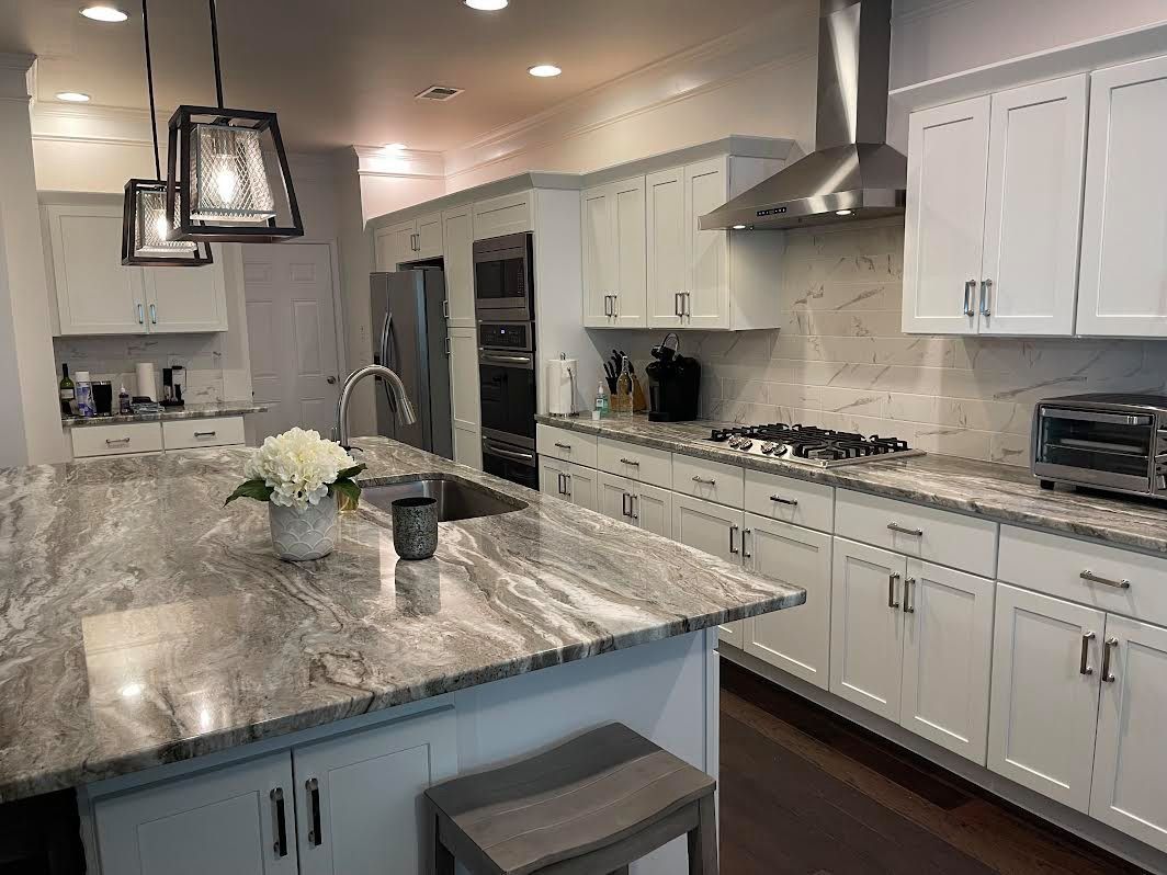 A modern kitchen with white cabinets, a large granite island, and stainless steel appliances.