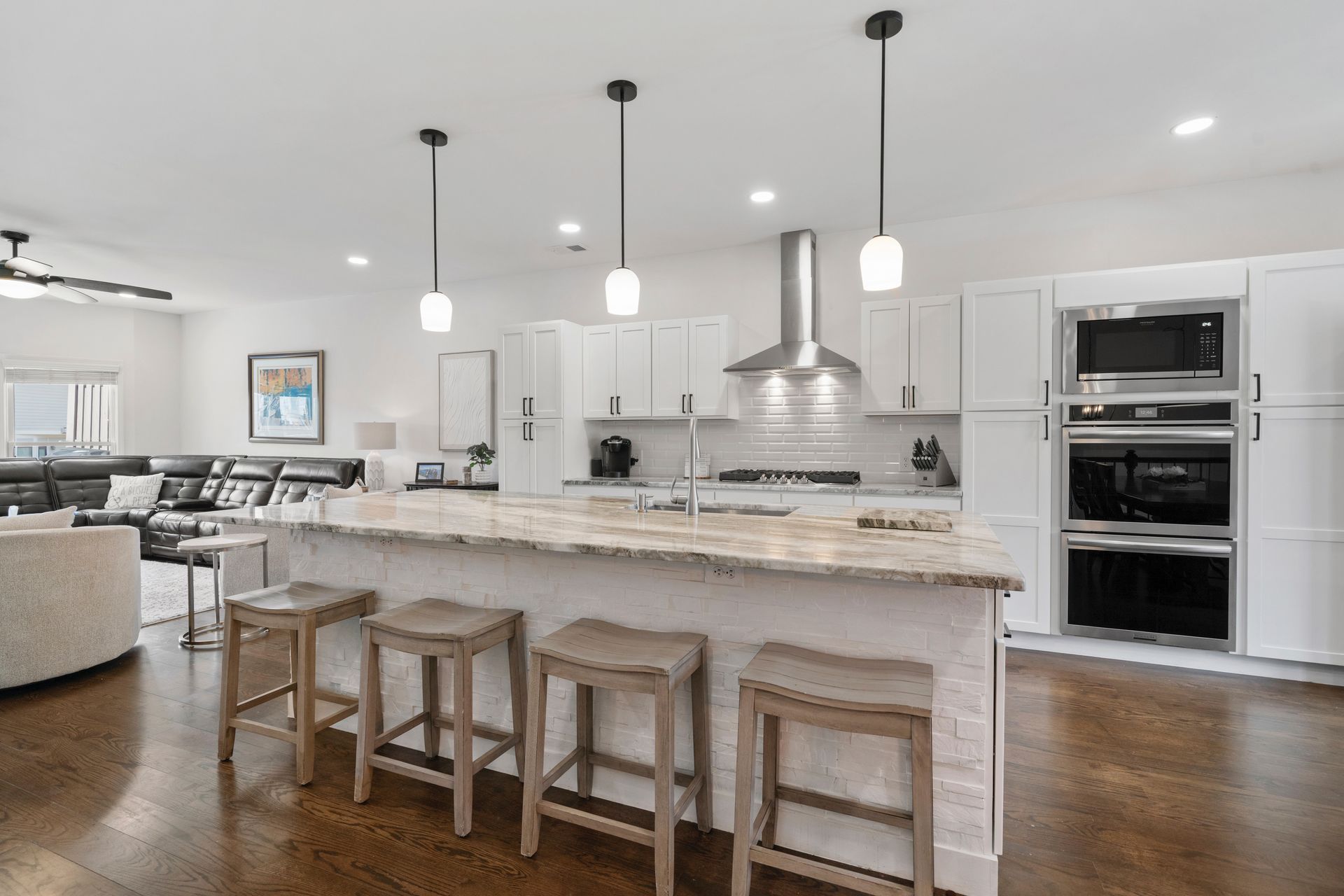 A modern kitchen with a large island, white cabinets, and stainless steel appliances. Four wooden bar stools sit at the island.