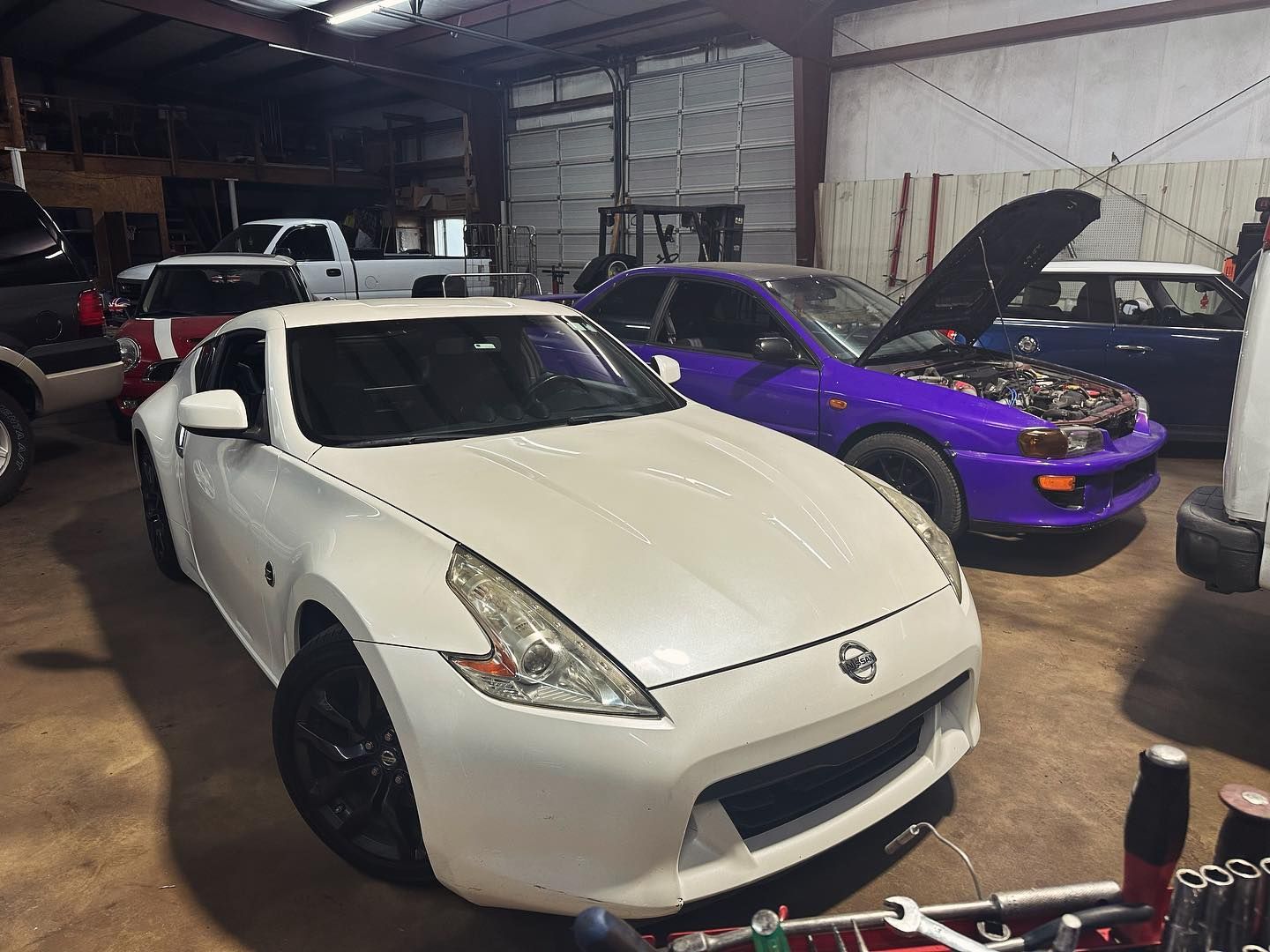 A white car is parked in a garage next to a purple car.