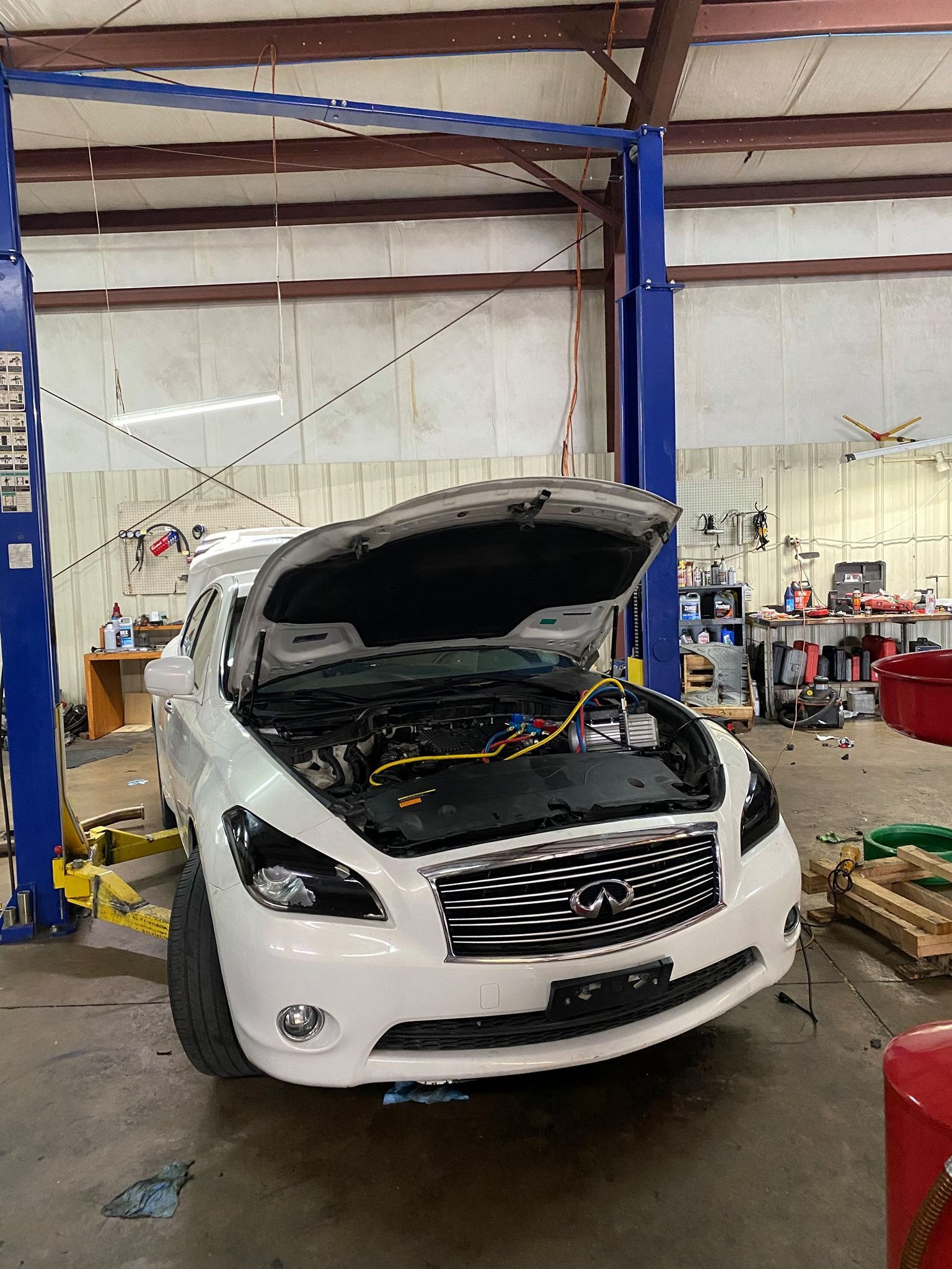 A white car with the hood open is sitting on a lift in a garage.