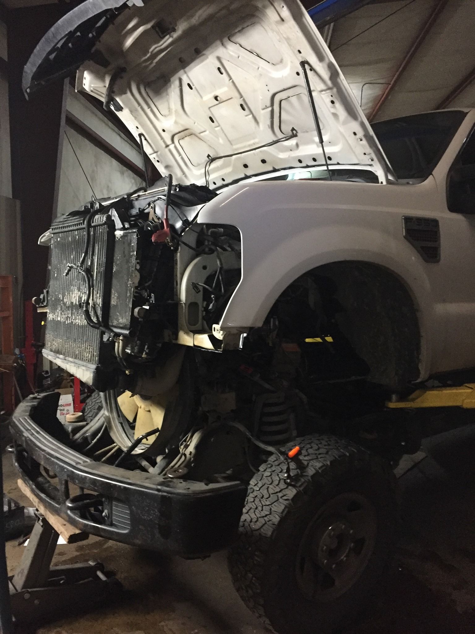 A white truck with the hood open is sitting in a garage.