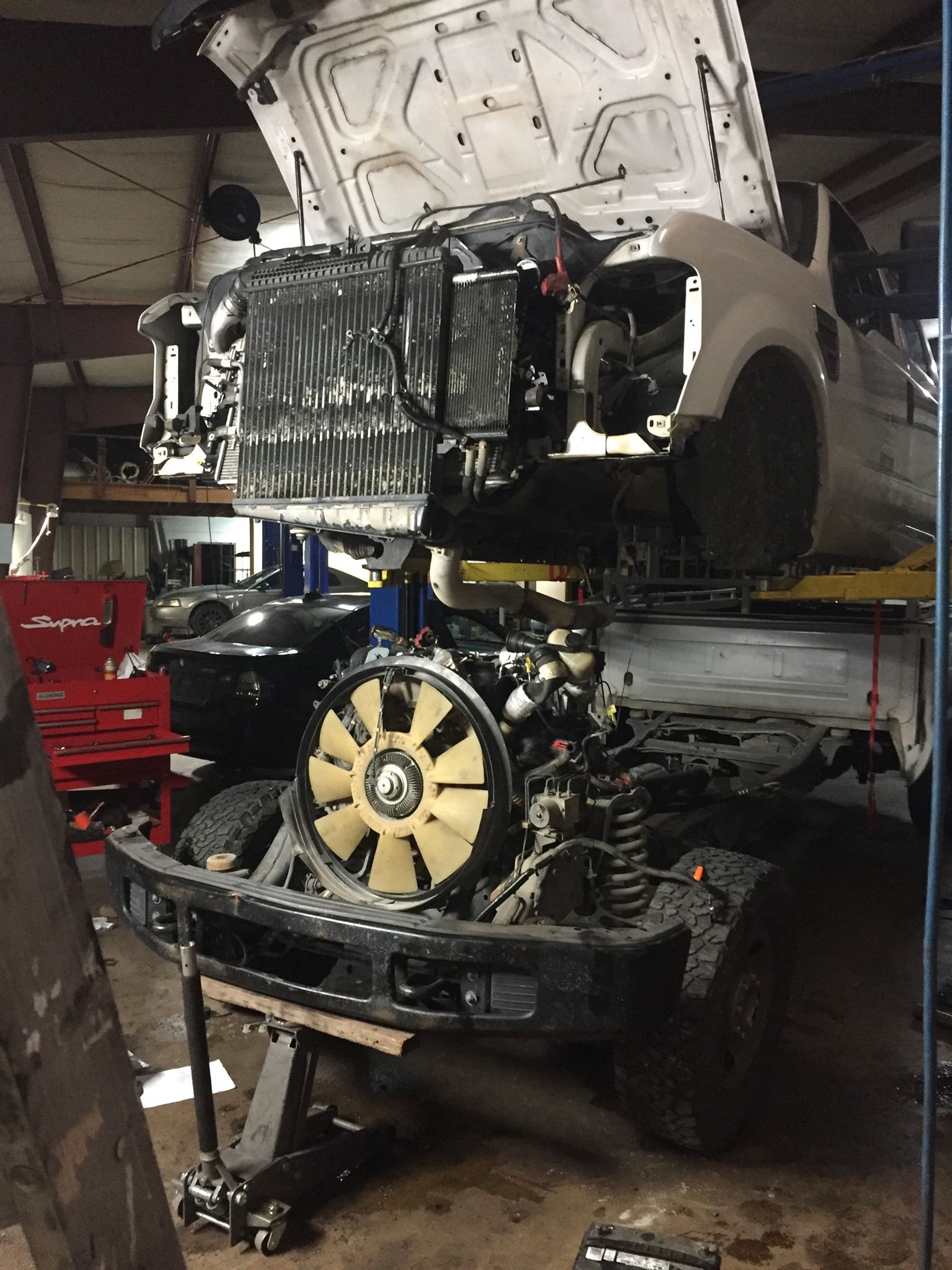 A car with the hood up is being worked on in a garage.