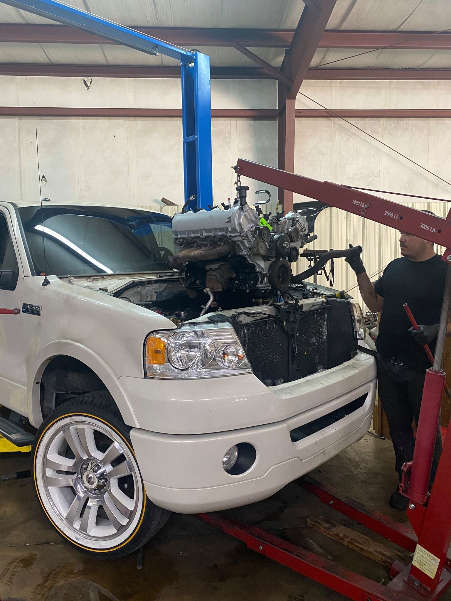 A white truck is being repaired in a garage with the hood open.