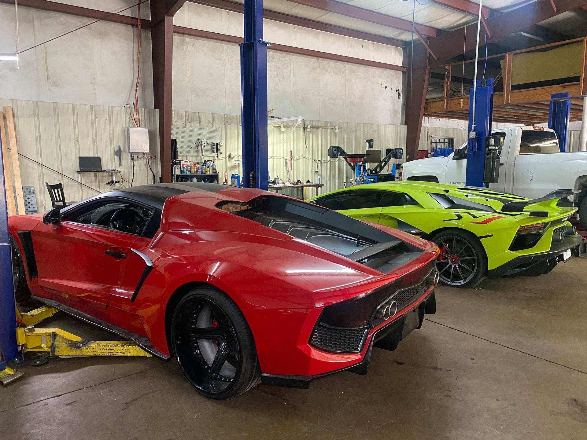 A red sports car is parked next to a green sports car in a garage.