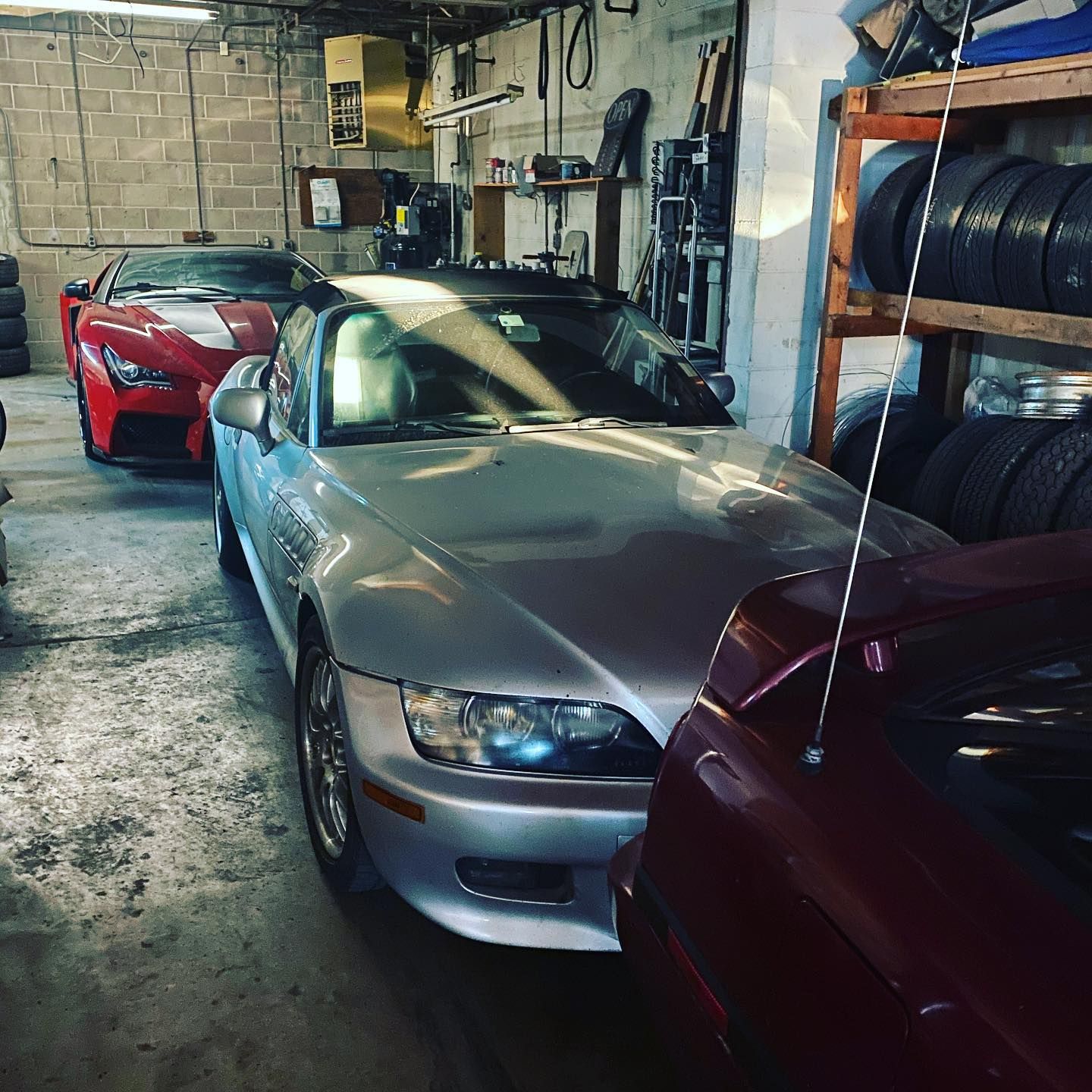 A silver car is parked in a garage next to a red car