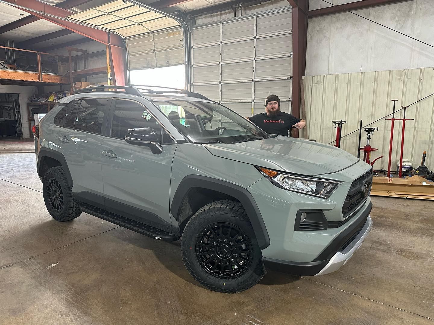 A man is standing next to a gray suv in a garage.