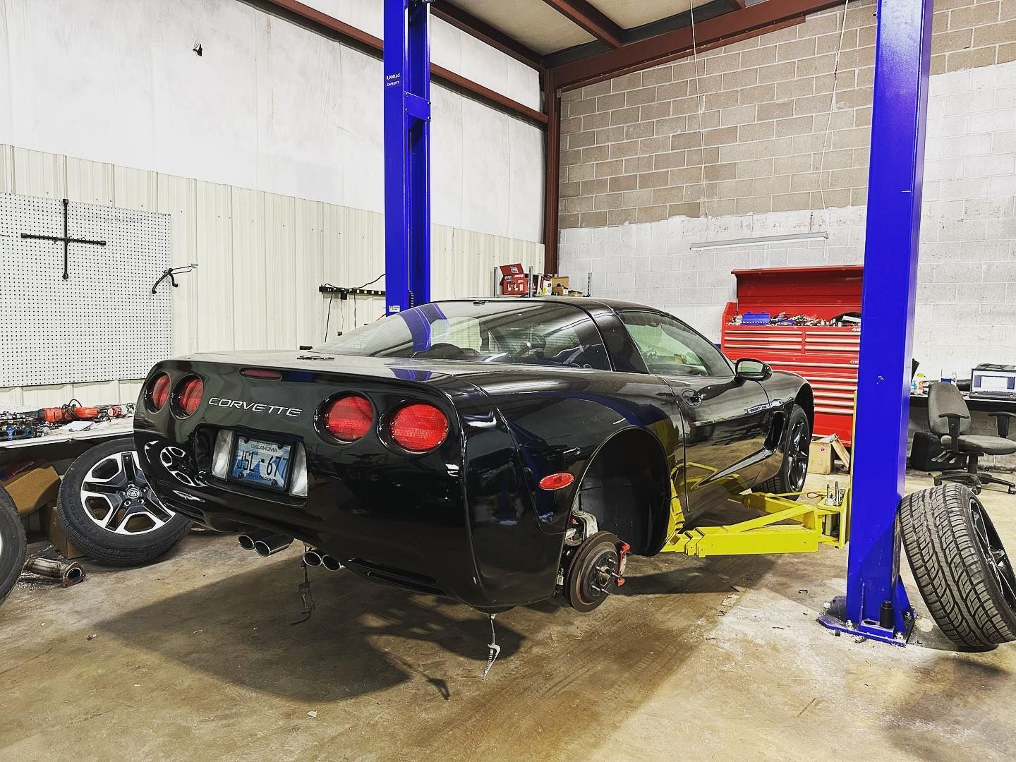 A black corvette is sitting on a lift in a garage.