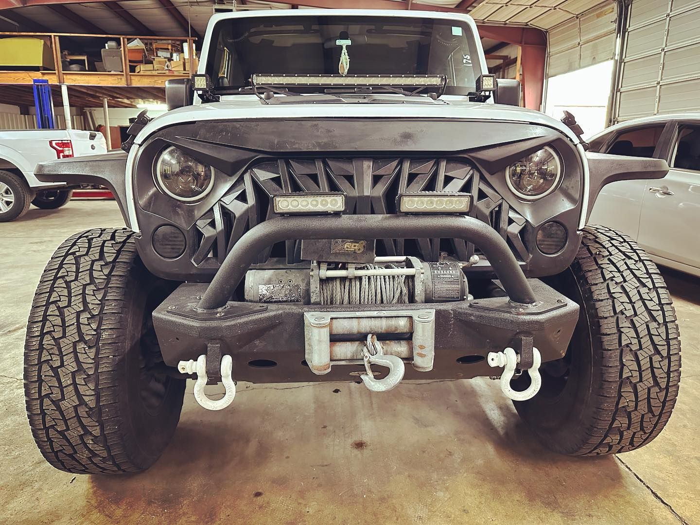 A jeep is parked in a garage with a winch attached to the front bumper.