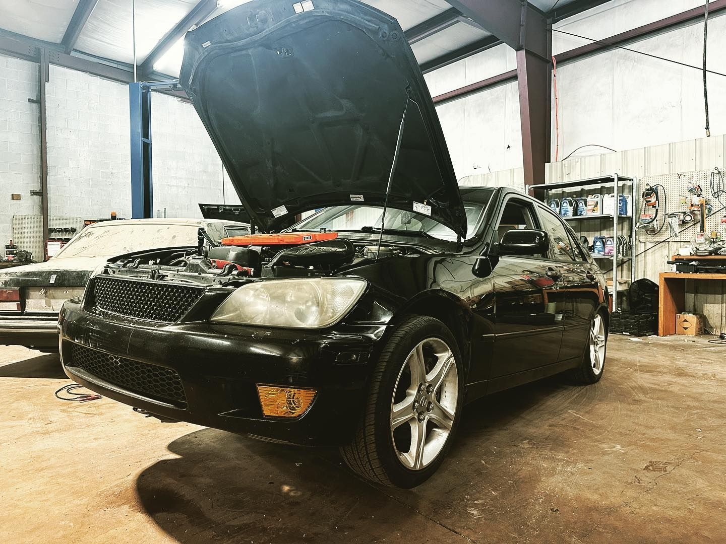 A black car with the hood up is parked in a garage.