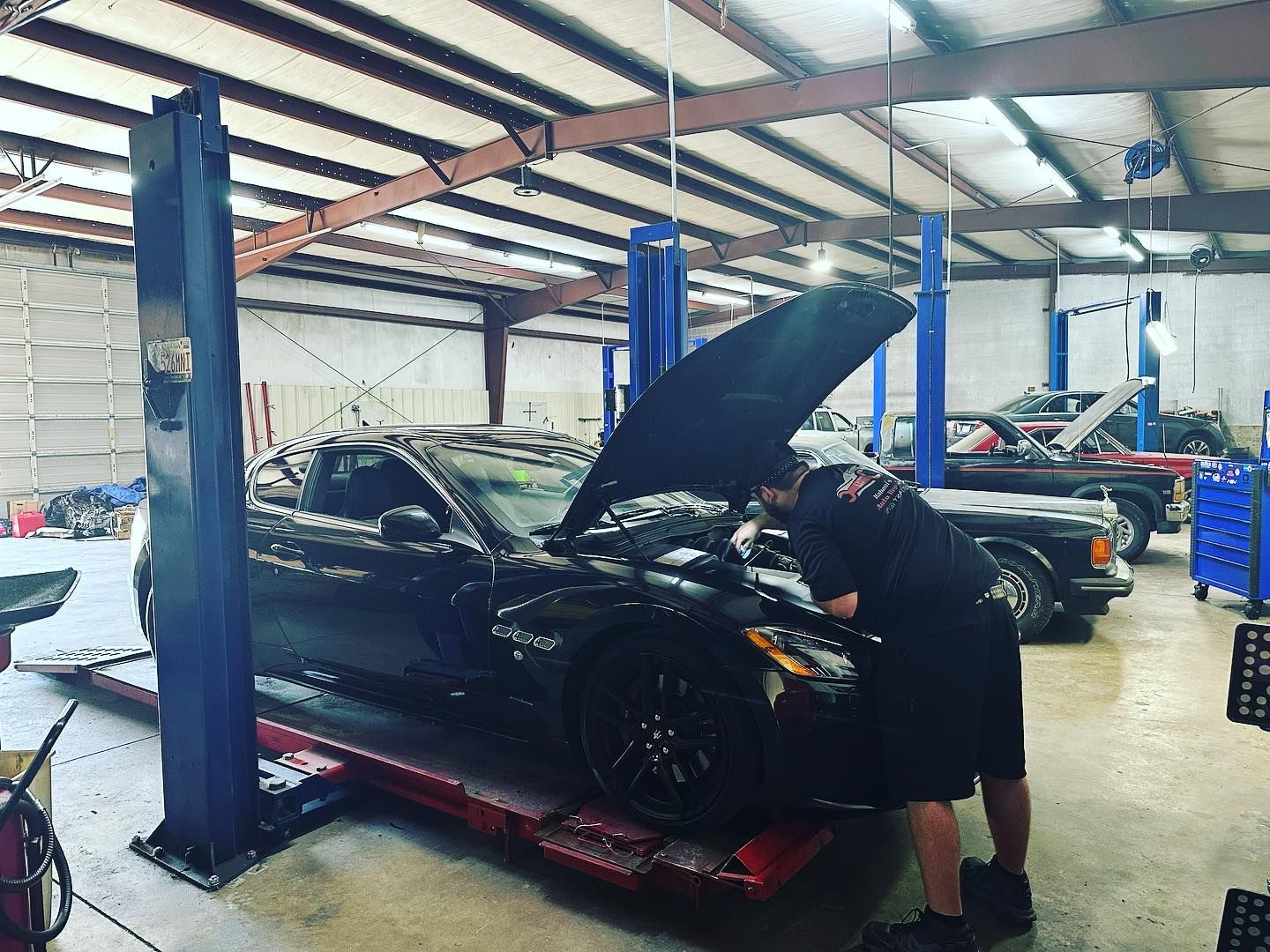 A man is working on a car in a garage with the hood up.