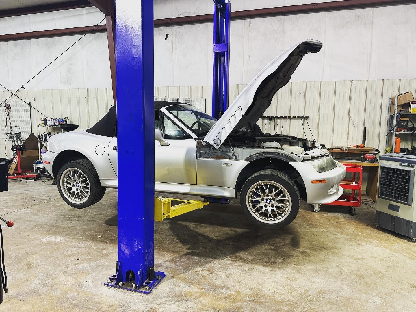 A silver car is on a lift in a garage with its hood up.