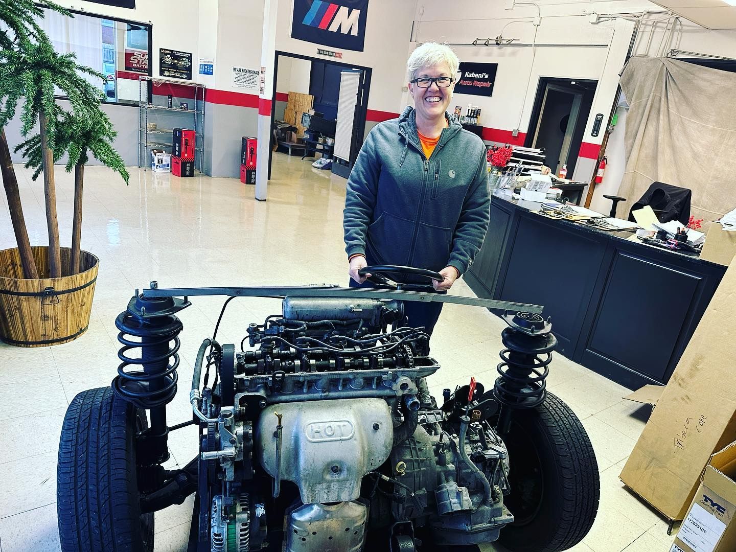 A woman is standing next to a car engine in a garage.