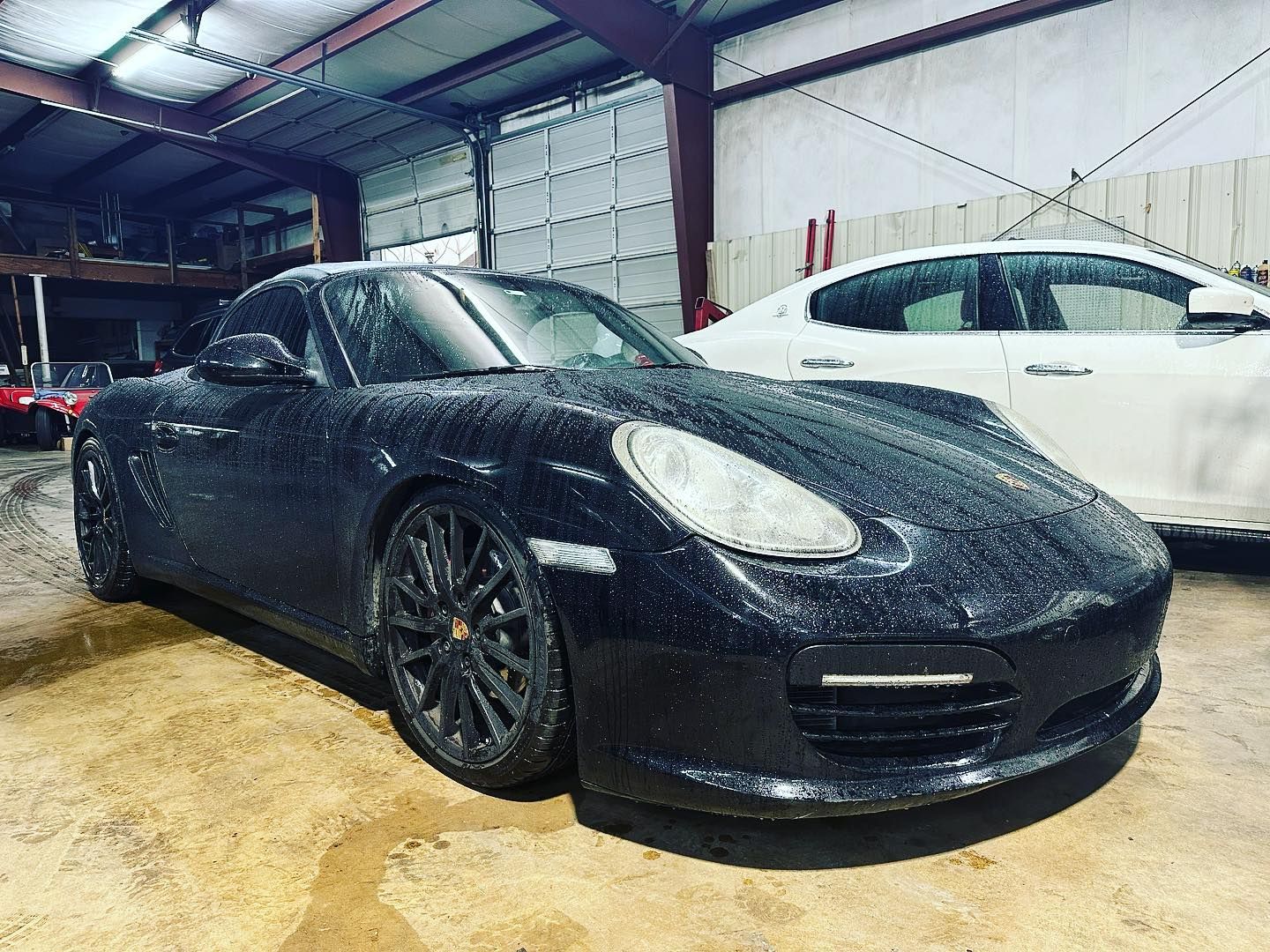 A black porsche boxster is parked in a garage next to a white car.